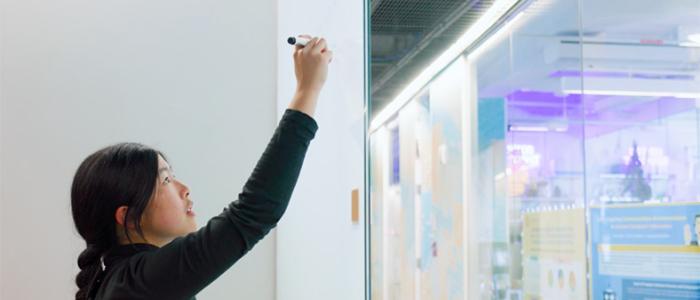 Student writing on a whiteboard in a research space.